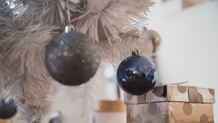 Silver polka dot giftbox placed under a white christmas holiday tree with shiny blue baubles.の写真素材