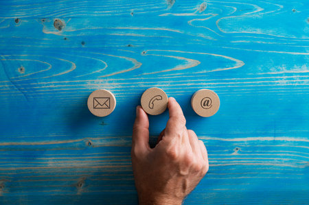 Male hand placing three wooden cut circles with contact and communication icons on them in a row over textured blue wooden background.の写真素材