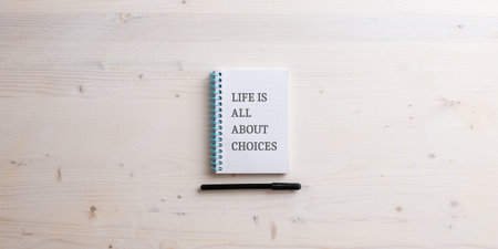 Spiral notebook with a Life is all about choices sign written in it. Black marker lying underneath it. Top view over wooden background.の写真素材