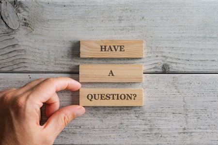 Male hand stacking three wooden pegs with a Have a question sign on them. Over white wooden background.の写真素材