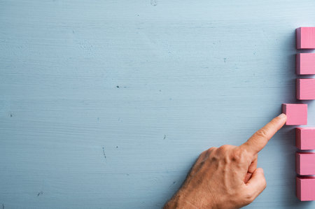 Male hand pushing a pink wooden block into a stack of them on the right side of an image with plenty of blue copy space on the left.の写真素材