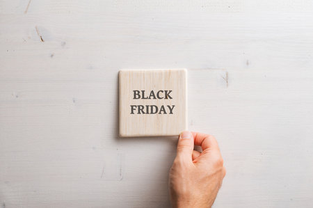 Male hand placing a wooden tile with a Black friday sign on it over a simple wooden background.の写真素材
