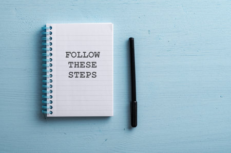 Spiral notebook with a Follow these steps sign placed over pastel blue wooden background with a black marker next to the notepad. With copy space on the right side of an image.の写真素材