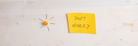 Wide view image of a yellow paper with Dont worry sign on it placed on wooden background with a sun made of smashed yellow paper and handdrawn rays.の写真素材