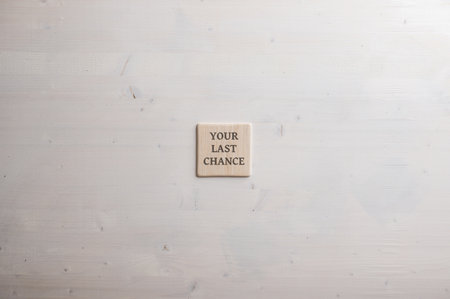 Wooden tile with an Your last chance written on it placed over plain wooden background with plenty...