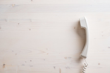 Simple white landline telephone handset placed on plain wooden background with plenty of copy space on the left side of an image.の写真素材