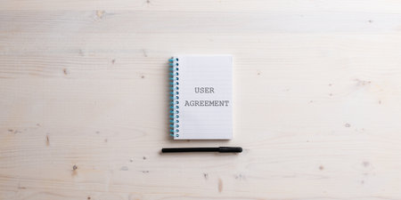 Spiral notebook with a User agreement sign written in it placed over simple wooden background with black marker under the notepad.の写真素材