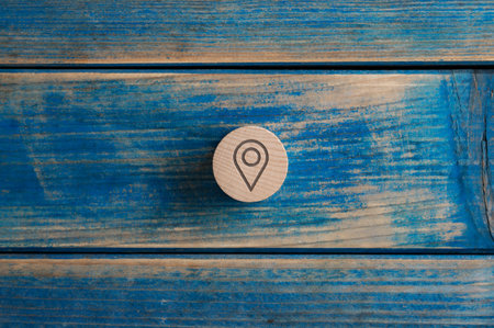 Wooden cut circle with a location icon on it placed over textured blue wooden background.の写真素材