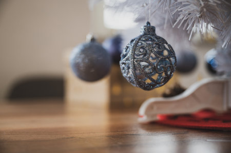 Low angle closeup view of shiny blue holiday baubles hanging from a white christmas tree standing on domestic table.の写真素材