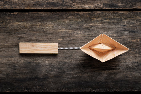 Origami boat made of orange polka dot paper pulling a blank wooden peg over rustic wooden background.の写真素材