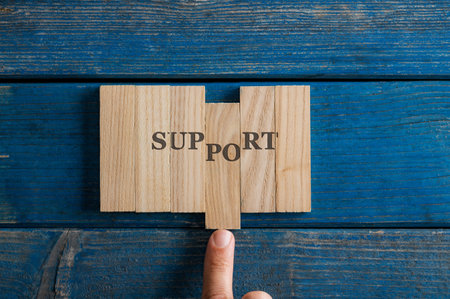 Male finger assembling a Support sign spelled on wooden pegs placed on rustic blue wooden boards.の写真素材