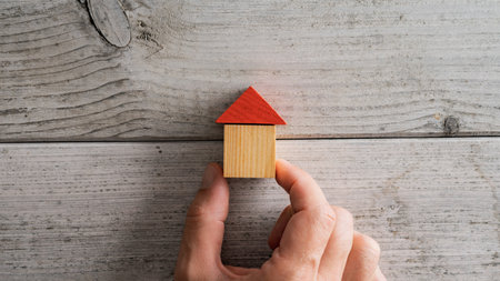 Male hand placing a house made of wooden blocks over a textured white wooden background.の写真素材