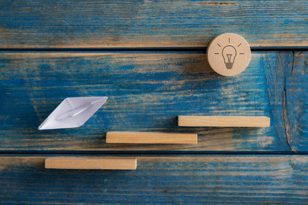 Conceptual image of vision, effort and determination - paper made origami boat sailing up a wooden...