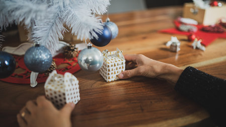 Closeup view of female hands preparing a holiday setting by placing small christmas gift boxes under a white tree with blue holiday baubles on it.の写真素材