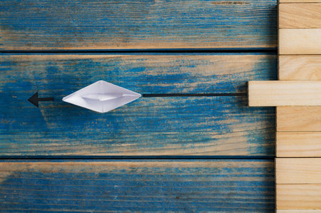 Conceptual image of uniqueness and personal vision - origami boat pulling a blank wooden peg out of a stack of them over blue background.の写真素材