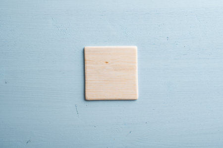 Simple plain blank wooden tile placed over pastel blue wooden background.の写真素材