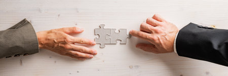 Top view of male and female business partners matching two blank puzzle pieces over simple wooden background. Wide view image.の写真素材