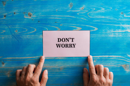 Male hands placing a pink paper with Dont worry sign on it over a textured blue wooden background.の写真素材