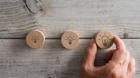 Male hand placing three wooden cut circles with light bulb icon drawn on them over textured white wooden background.の写真素材