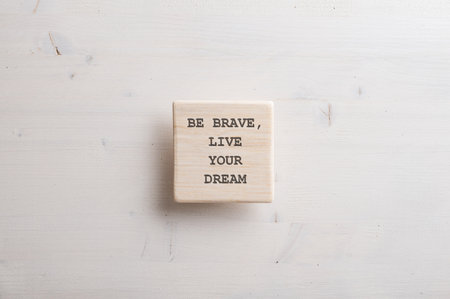 Wooden tile with a Be brave live your dream sign written on it placed over plain simple wooden background.の写真素材