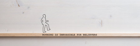 Wide view image of a silhouette of a man walking across a wooden slat with a Nothing is impossible for believers sign on it placed over plain simple wooden background with copy space.の写真素材