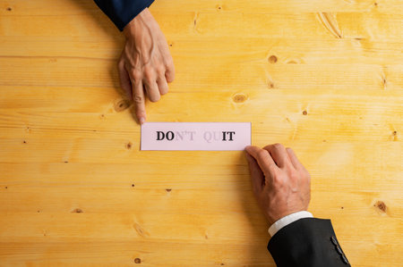 Hand of male and female businesspeople holding a pink paper with a Dont quit sign fading into a Do it message. Over yellow wooden background.の写真素材