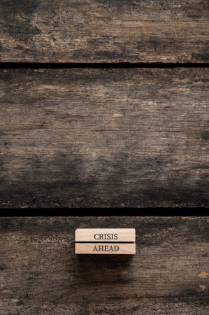 Two stacked wooden pegs with a Crisis ahead sign on them placed over textured rustic wooden background. With plenty of copy space on the top part of the image.の写真素材