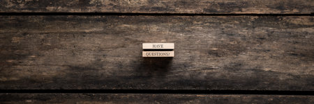 Wide view image of two stacked wooden pegs with a Got questions? sign on them placed over textured rustic wooden background.の写真素材