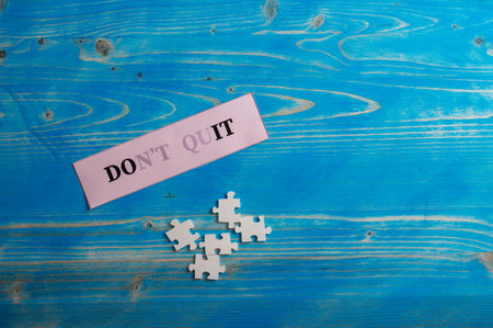 Scattered puzzle pieces placed next to a pink paper with a Dont quit sign fading into a Do it sign. Over textured blue wooden background.の写真素材