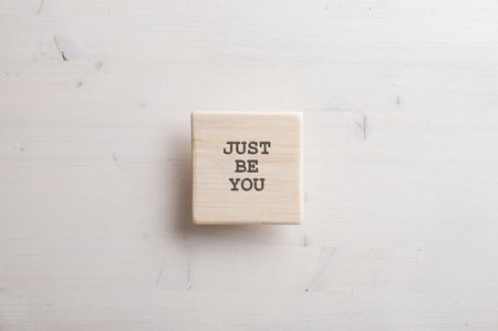Simple wooden tile with a Just be you sign on it placed over plain wooden background.の写真素材