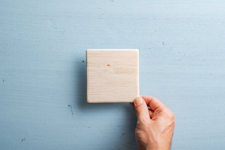 Male hand placing blank wooden tile over a pastel blue background. With copy space.の写真素材