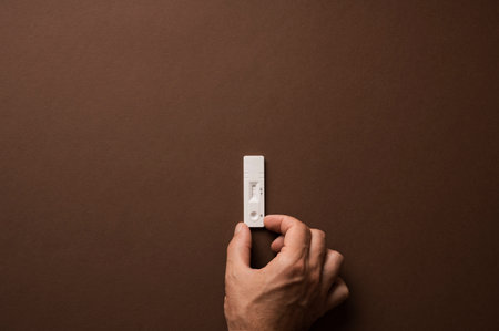 Male hand placing positive testing plate for coronavirus on a brown background. With copy space.