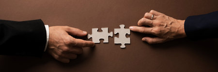 Wide view image of businessman and businesswoman hands joining two blank matching puzzle pieces. Over brown background.の写真素材