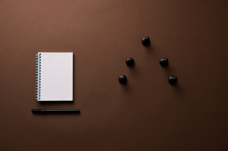 Blank spiral notebook with a black pen next to six black pawn chess pieces in a conceptual image of strategy and planning. Over brown background.の写真素材