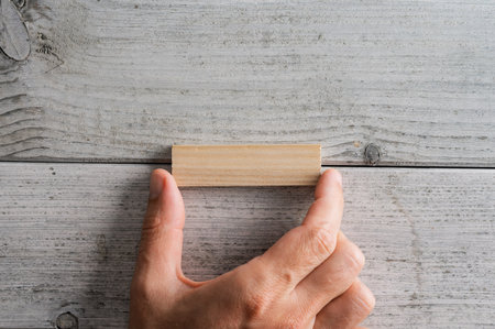 Top view of male hand placing a blank wooden peg on white textured wooden background.の写真素材