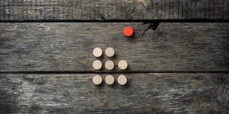Red wooden cut circle placed away from a group of plain round circles in a crowd. Over textured wooden background.の写真素材