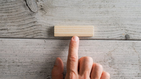 Male finger pointing to a blank simple wooden peg placed over white textured wooden background.の写真素材