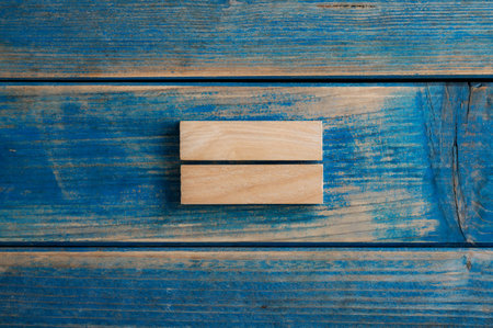 Two simple blank wooden pegs stacked one on top of the other placed over textured blue wooden background.の写真素材
