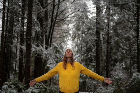 Peaceful young woman in vibrant yellow sweater practicing mindfulness standing in winter forest.の写真素材