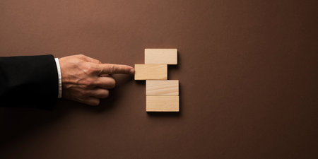 Hand of a businessman pushing a simple blank wooden peg in a stack of them. Over brown background.の写真素材