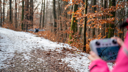 Rear view of a woman managing a drone floating in front of her with remote controller outside in...