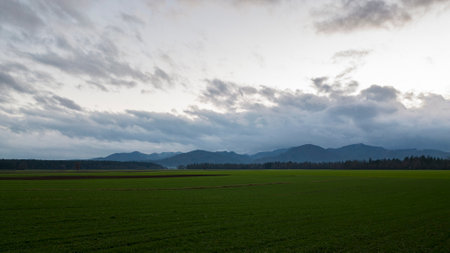 Beautiful green landscape with farmland and mountains in the distance under a dramatic cloudy sky.の写真素材