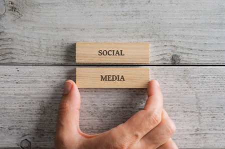 Male hand stacking two wooden pegs with a Social media sign on them. Over textured white wooden background.の写真素材