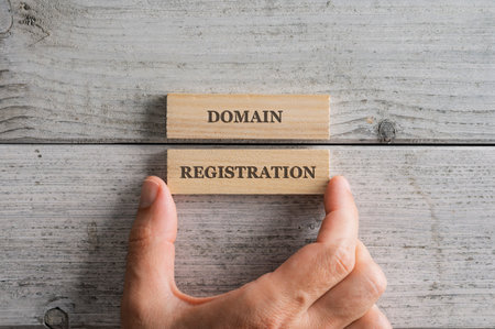 Male hand stacking two wooden blocks with a Domain registration sign on them. Over white textured...