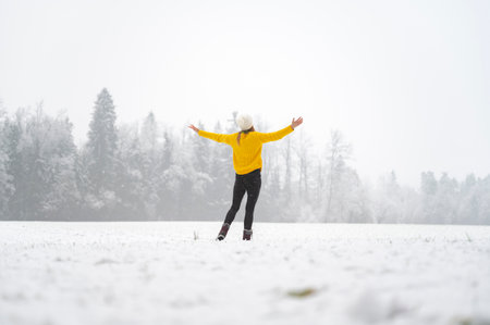 Young woman in a vibrant yellow sweater standing with her arms open outside in whinter nature on a snowy day.の写真素材