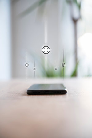 Low angle view of a black mobile phone placed on a desk with a globe icons coming out of it in a conceptual image of global connectivity, internet and communication.の写真素材