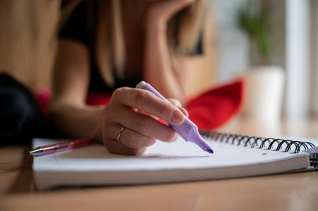 Low angle closeup view of female hand about to highlight something in her notebook with a purple marker. Student learning and studying.の写真素材