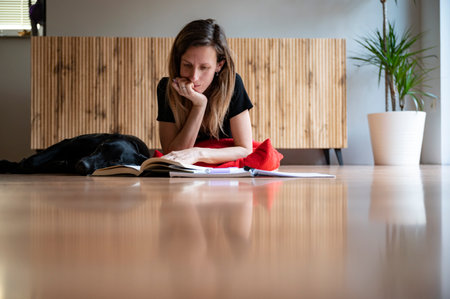 Young woman, a student, lying on a living room floor studying with her notebook and books open in front of her and er black dog lying next to her.の写真素材