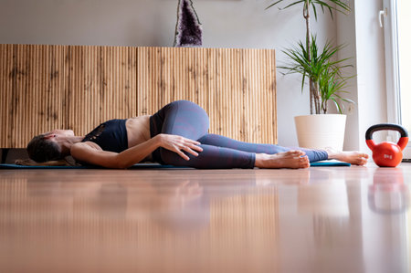 Young woman lying on the mat on the floor making stretching exercise after a home workout routine.