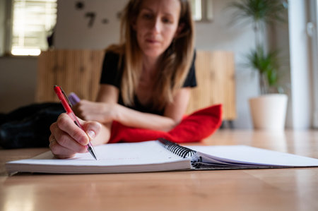 Low angle view of a young woman, a student, studying and writing in her notebook as she is lying on...